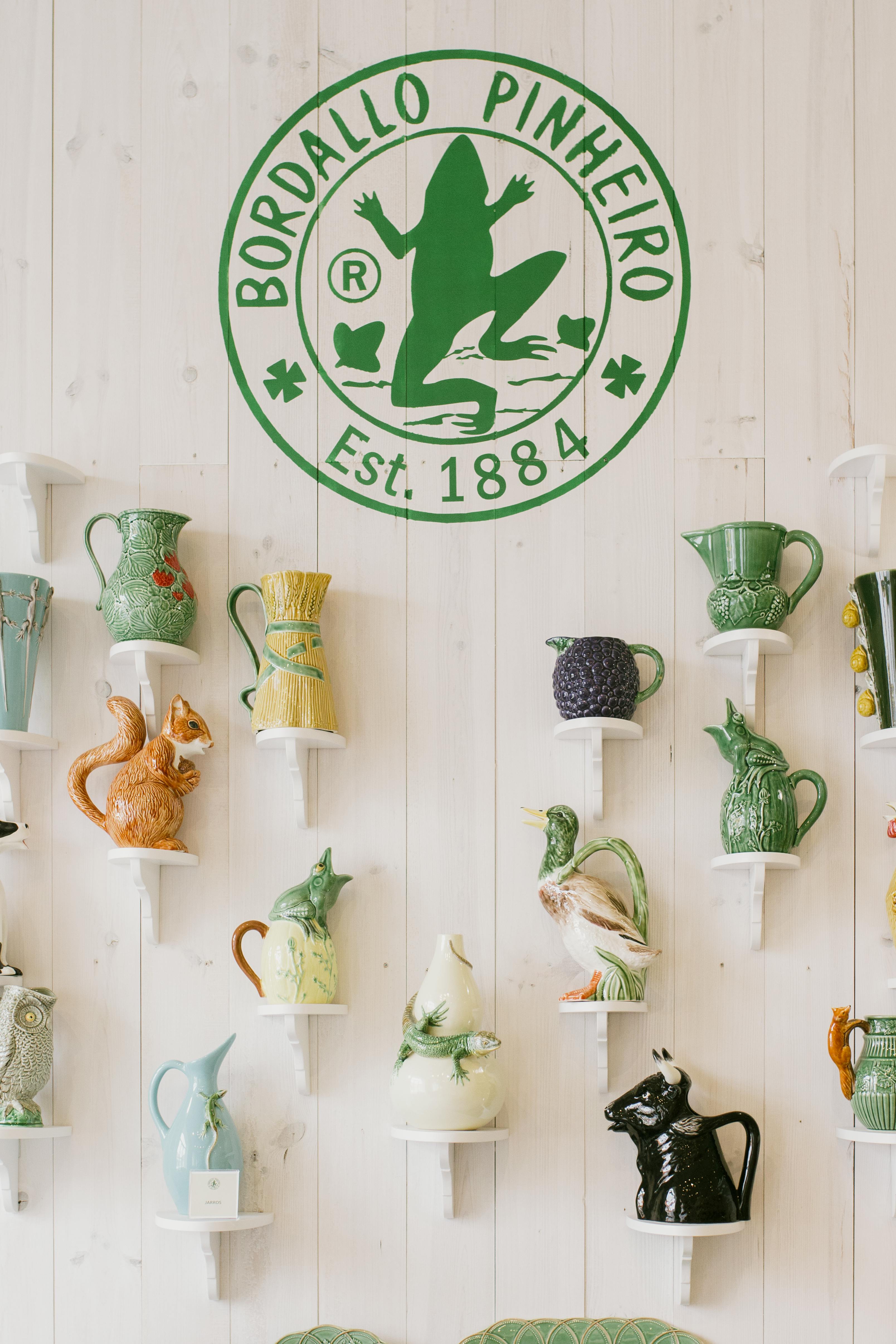 Vibrant collection of Bordallo Pinheiro ceramic decorations on white wall shelving.