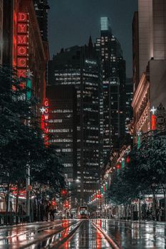 Vibrant nighttime street scene in Sydney with skyscrapers and colorful lights reflecting on wet pavement.