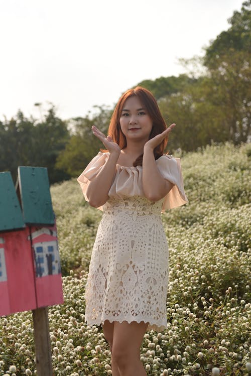 Woman in Lace Dress Standing next to Wooden Sign in Field of Flowers