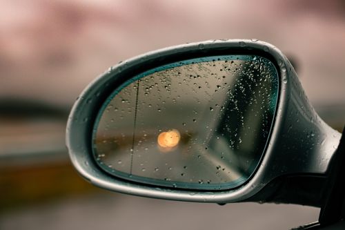Free Close-up of car side mirror with raindrops, reflecting blurred lights on a rainy day. Stock Photo
