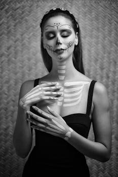 Black and white portrait of a woman with Día de los Muertos skull makeup, eyes closed.