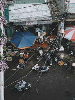 A bustling street market scene in Dalat, Vietnam, featuring scooters, vendors, and vibrant umbrellas.