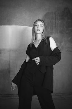 A fashionable young woman confidently posing in a black suit and blazer, exuding elegance.