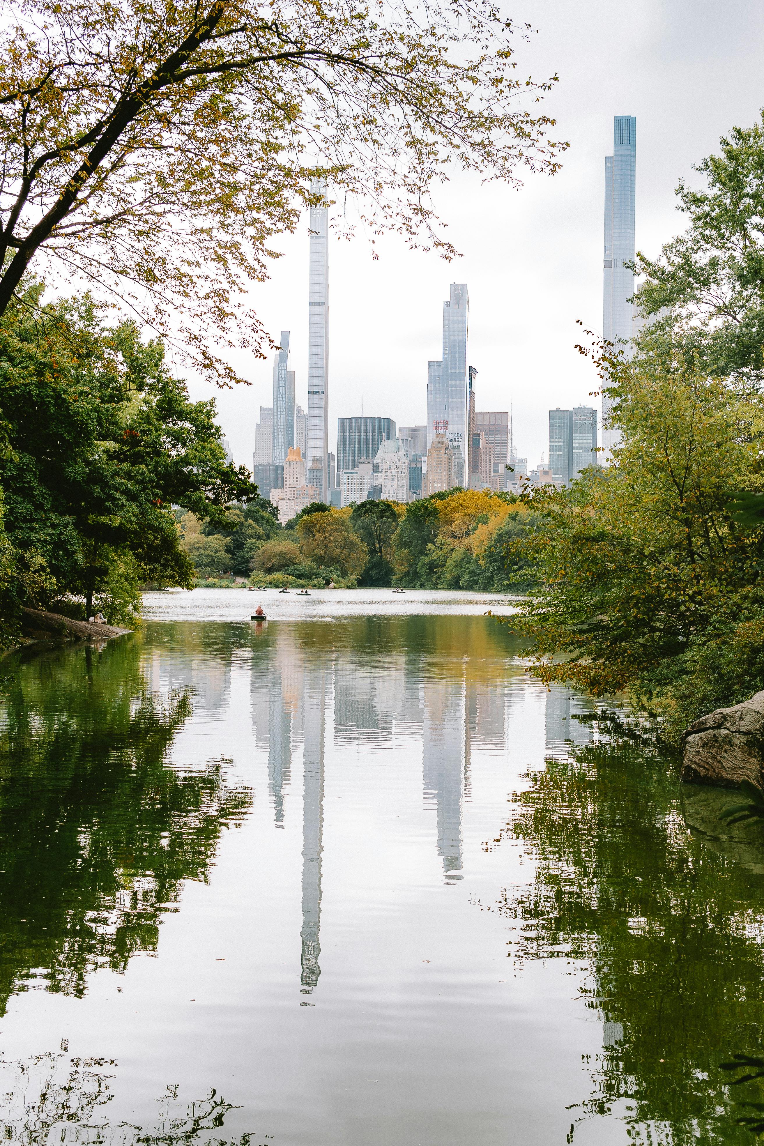 Capture of New York City's iconic skyline from Central Park, showcasing serene lake reflections and autumn foliage.