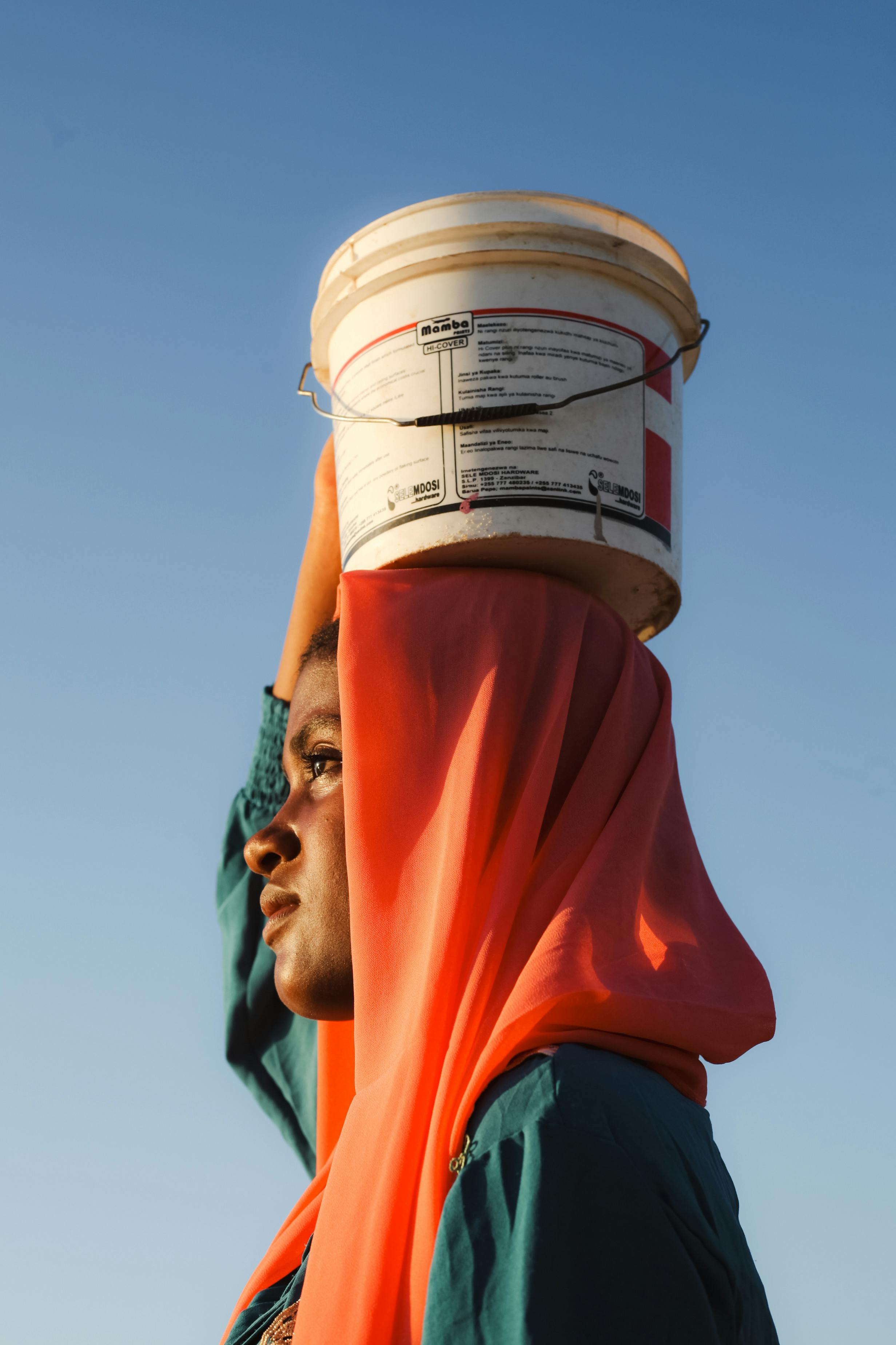 Young Woman in Headscarf Carrying Bucket on Head · Free Stock Photo