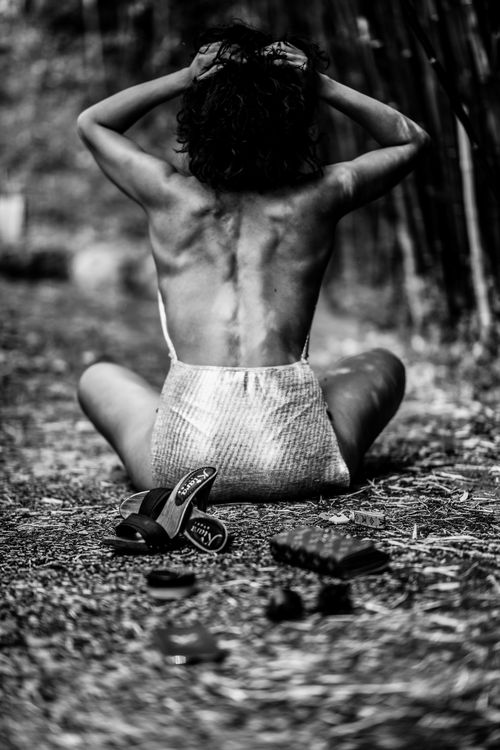 Free Monochrome image of a topless woman sitting back view, fixing hair outdoors. Stock Photo