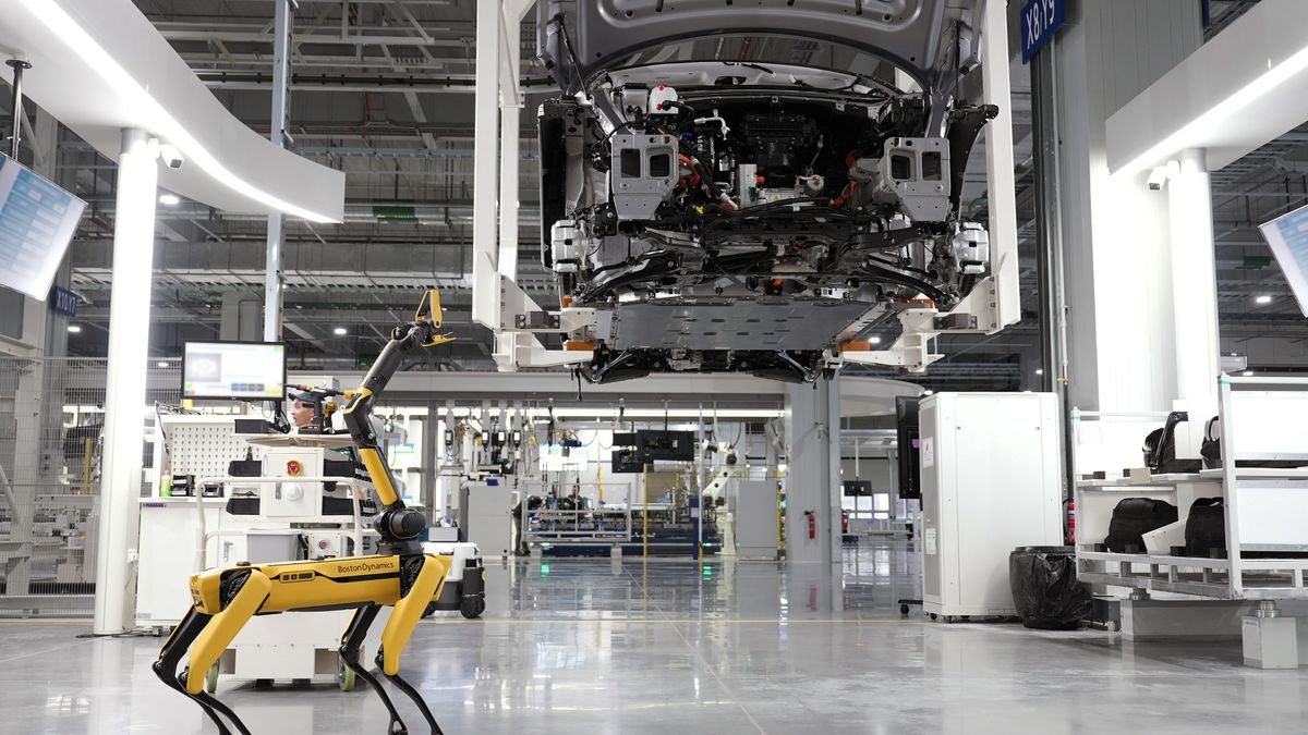 A robotic dog oversees an automated car assembly in a high-tech factory setting.