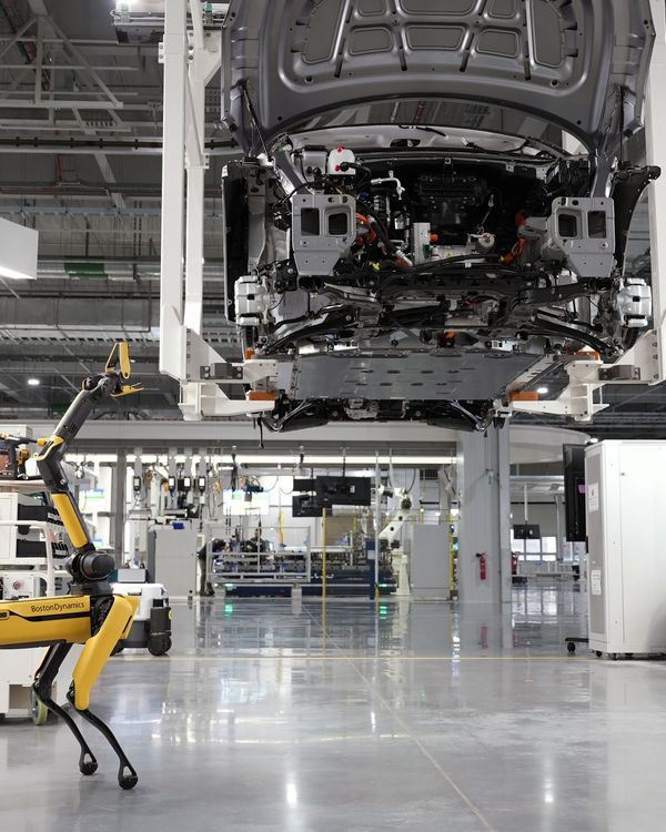 A robotic dog oversees an automated car assembly in a high-tech factory setting.