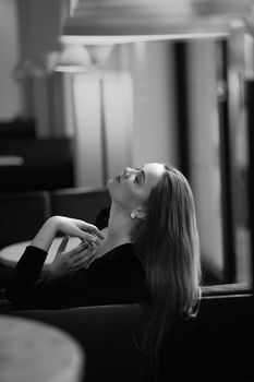 Black and white shot of a woman posing with eyes closed in a modern restaurant setting.