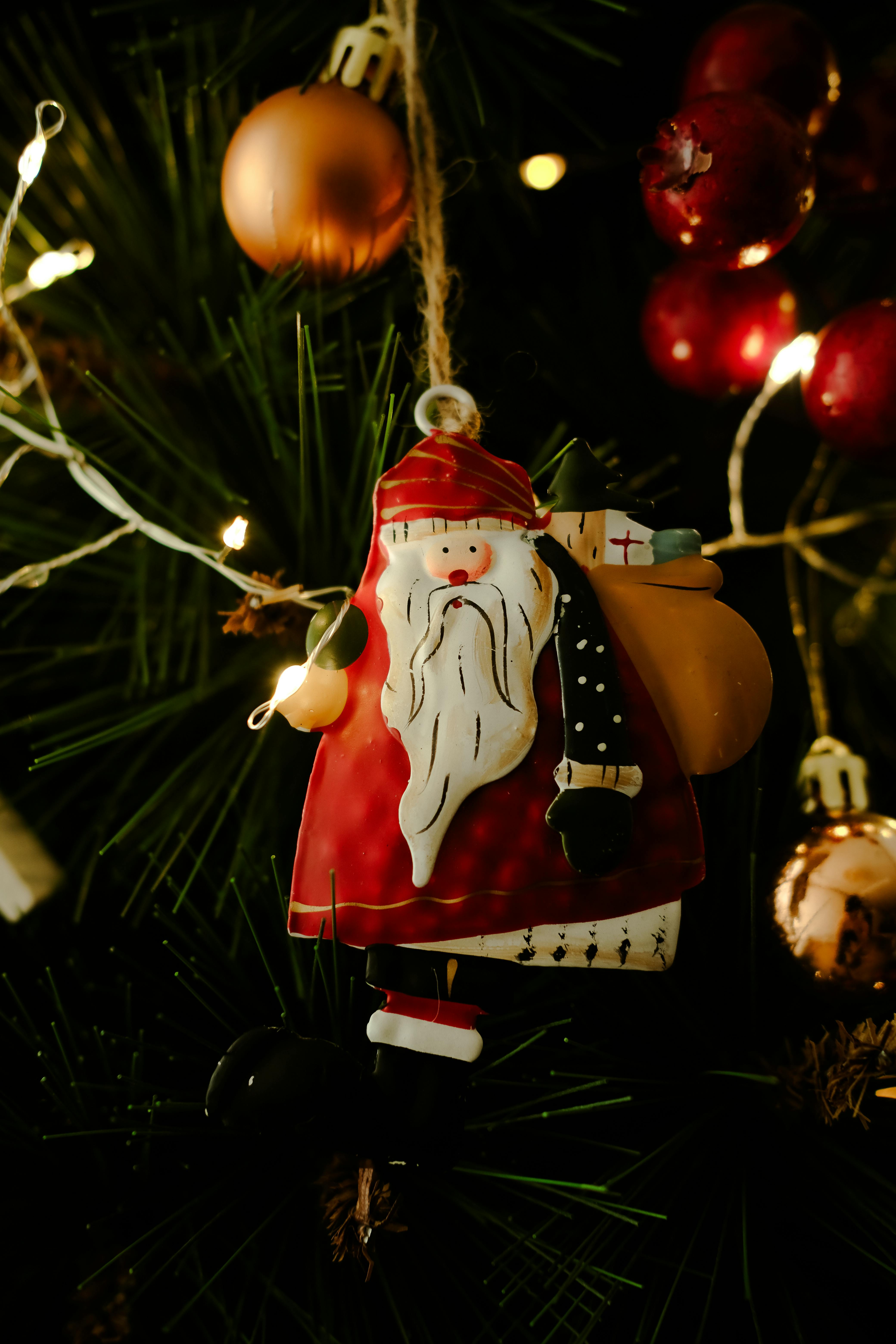 Close-up of a Santa Claus ornament hanging on a decorated Christmas tree with lights.