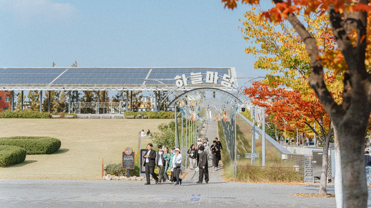 춘천 하루 — Visitors walking in a Korean park during autumn, surrounded by colorful foliage.