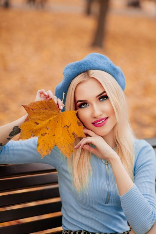 Free Stylish portrait of a woman in a blue beret holding an autumn leaf, captured outdoors. Stock Photo