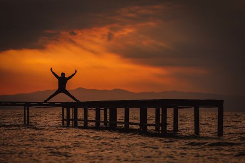 Free Silhouette of an adult stretching on a pier with a stunning sunset backdrop. Stock Photo