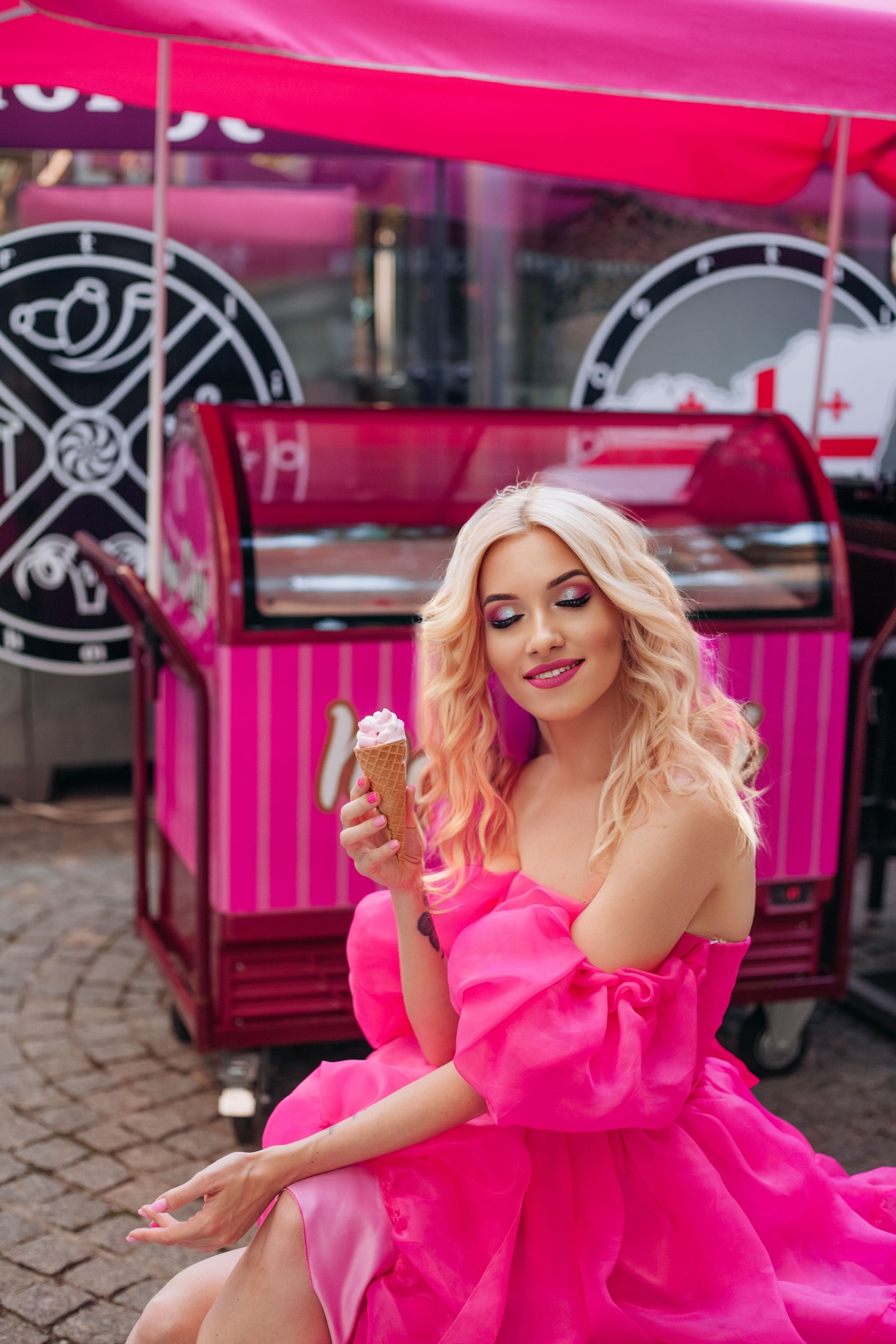 A blonde woman in a pink dress sitting on a bench · Free Stock Photo