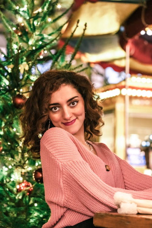 Smiling Woman in Pink Sweater by Christmas Tree
