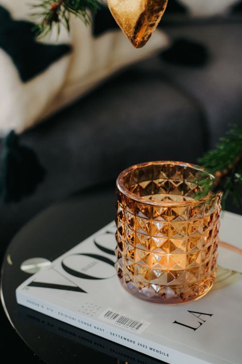 Free A stylish candle in a glass holder atop a fashion magazine, creating a cozy Christmas atmosphere. Stock Photo