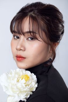 Close-up portrait of a stylish woman holding a white flower against a gray background.