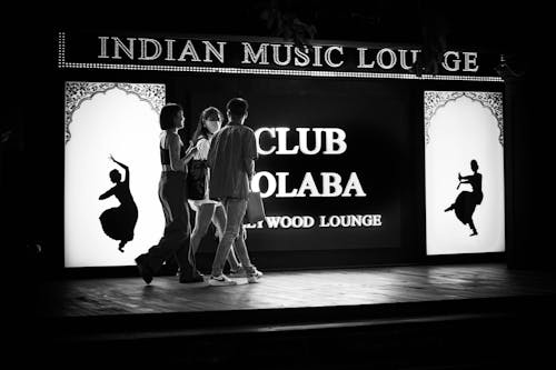 A Group of Young People Walking on a Sidewalk next to an Illuminated Sign of a Club 