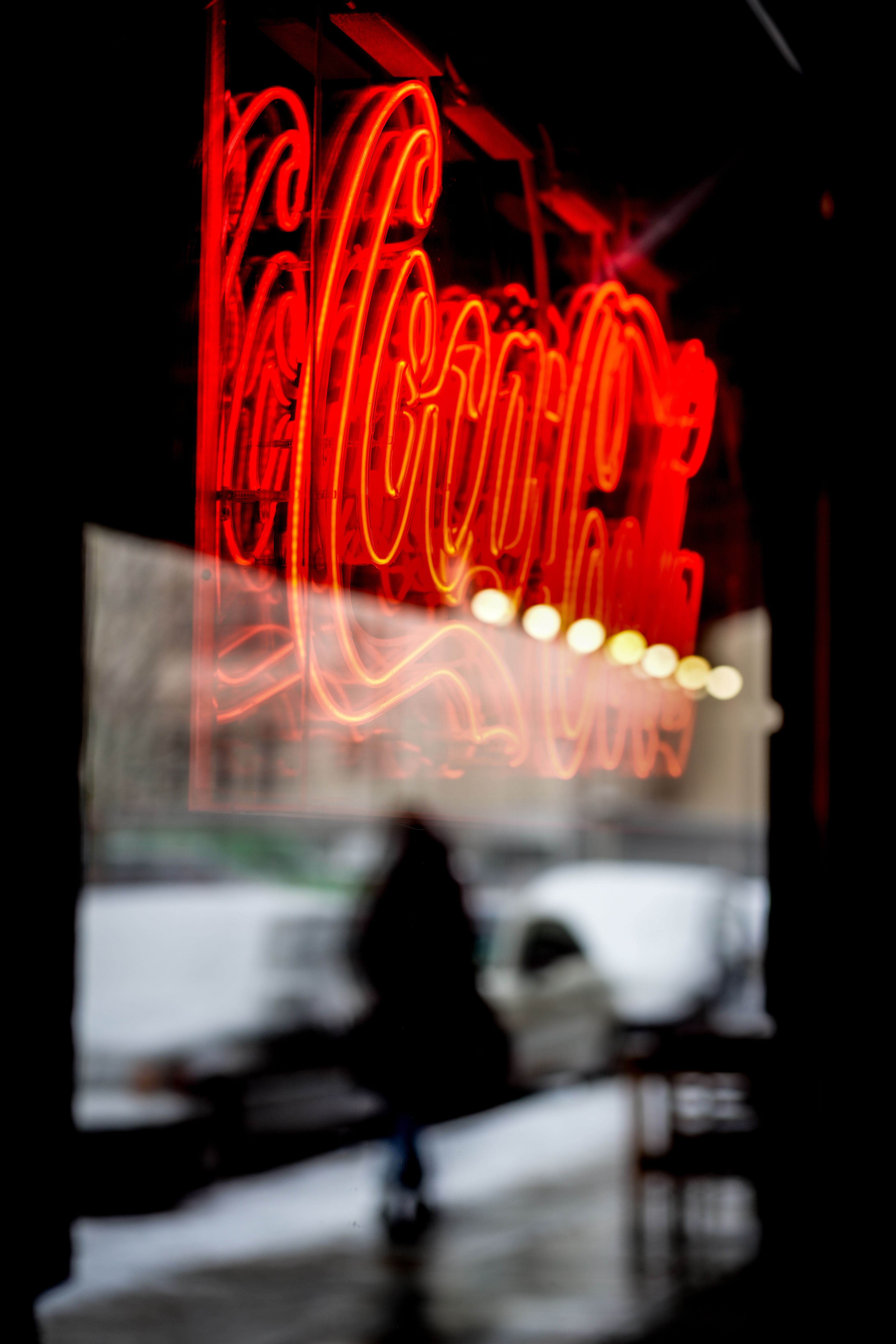 Vibrant red neon sign reflecting in a window at night, featuring a blurred figure outside.