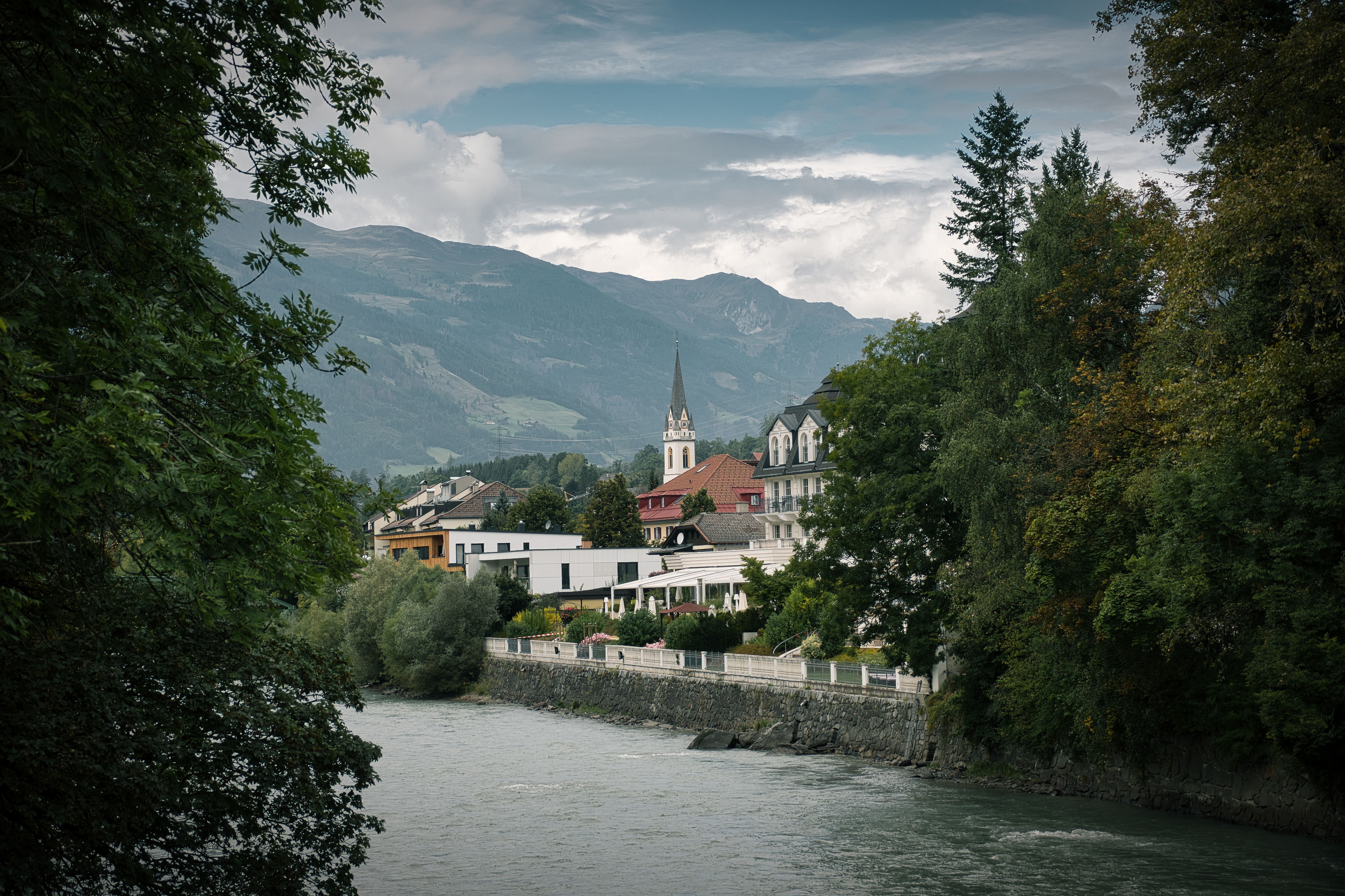 Scenic view of Lienz, Tirol featuring a river, mountains, and charming town architecture.