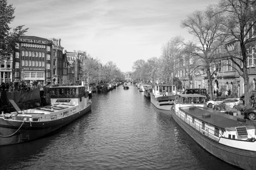 Free Scenic black and white view of Amsterdam canal with boats and classic architecture. Stock Photo