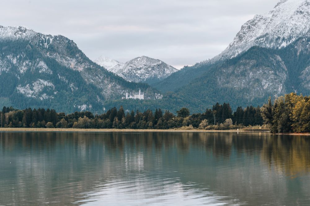 Castelul Neuschwanstein oglindit în Lacul Alpsee, cu Alpii înzăpeziți