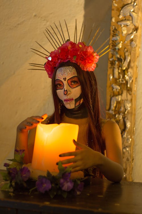 Photo of a Woman Dressed as a Catrina Sitting next to a Candle 