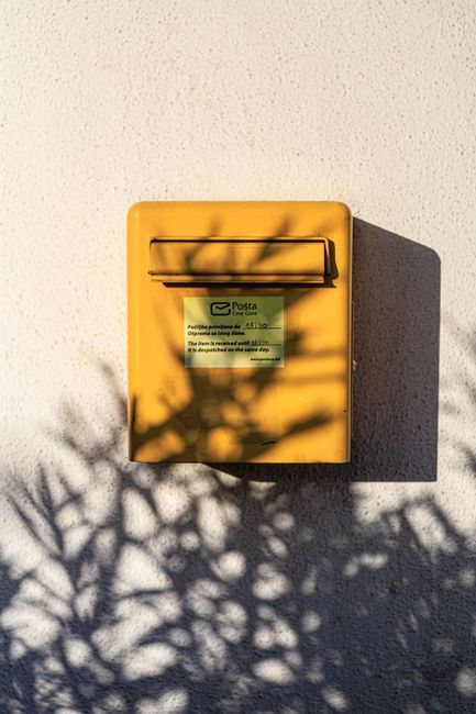 Sunlit yellow mailbox casting dramatic shadows on a textured wall outdoors.
