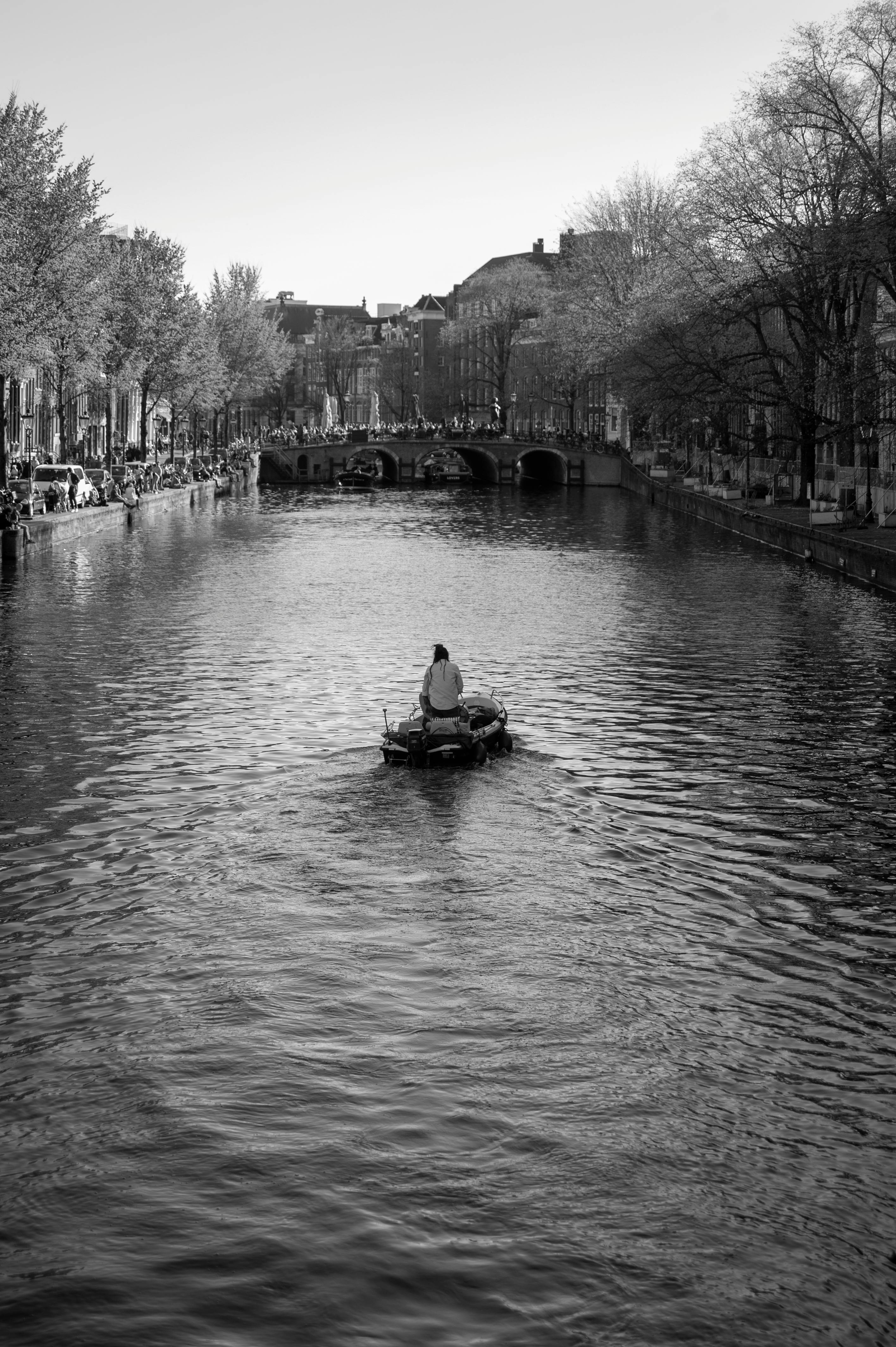 Person rowing on a peaceful canal with an arch bridge, in a city setting.