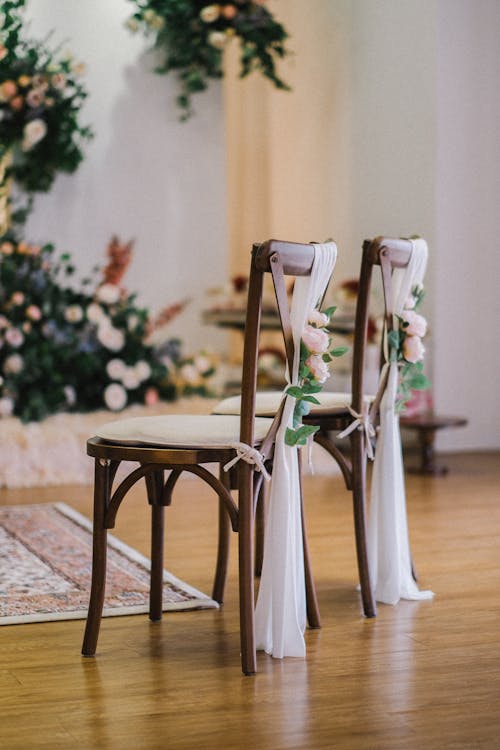 Two Chairs Decorated with White Fabric and Flowers 