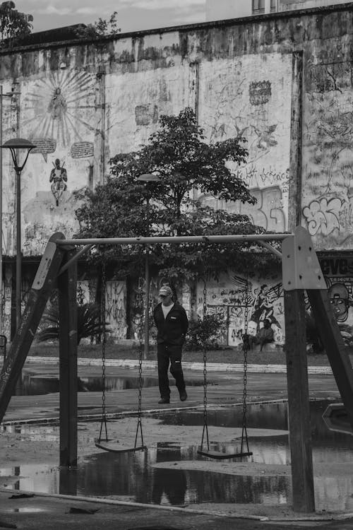 Free Black and White Photo of a Pedestrian Walking Past a Playground Stock Photo