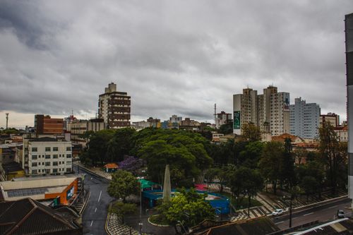 Free A vibrant cityscape featuring high-rise buildings and a lush park under a cloudy sky. Stock Photo