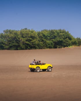 Yellow jeep driving through desert landscape under clear blue sky.