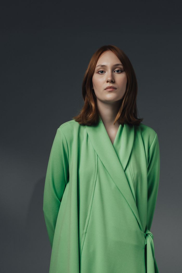 Portrait of a woman in a green coat against a dark studio wall. Photo by Matheus Bertelli on Pexels.