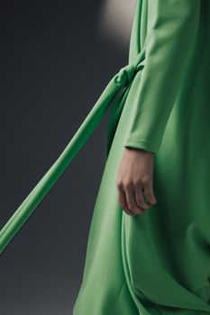 A close-up shot of a woman wearing a fashionable green dress against a gray background.