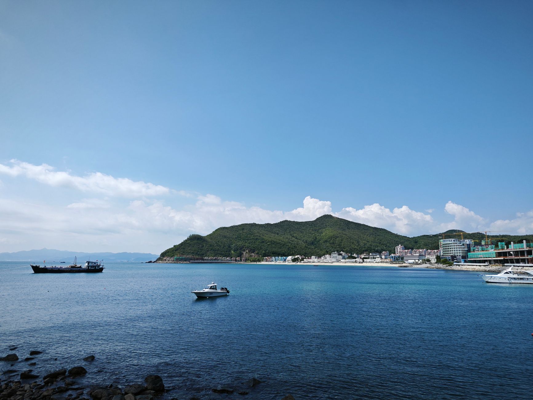 Serene coastal view featuring boats and lush green island under clear sky.