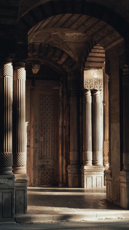 Free Sunlight streaming through a classical corridor with ornate columns and detailed woodwork. Stock Photo