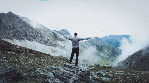 Free A man stands on a mountain peak with arms outstretched, embracing freedom. Stock Photo
