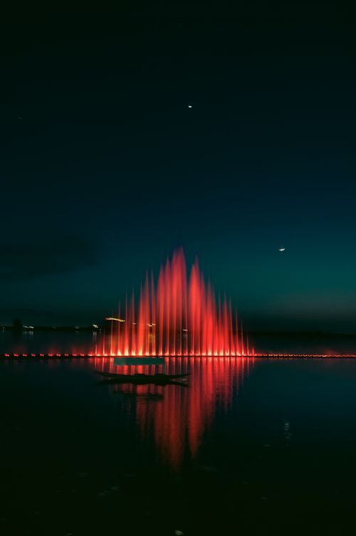Free A stunning red-lit fountain reflects in the calm waters under a night sky in Srinagar. Stock Photo
