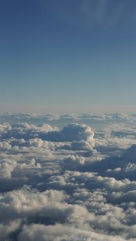 A serene aerial photo of fluffy white clouds against a clear blue sky at sunset.