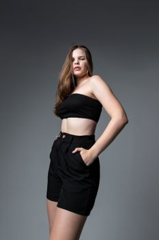Young woman in a stylish black outfit posing confidently indoors during a studio photoshoot.
