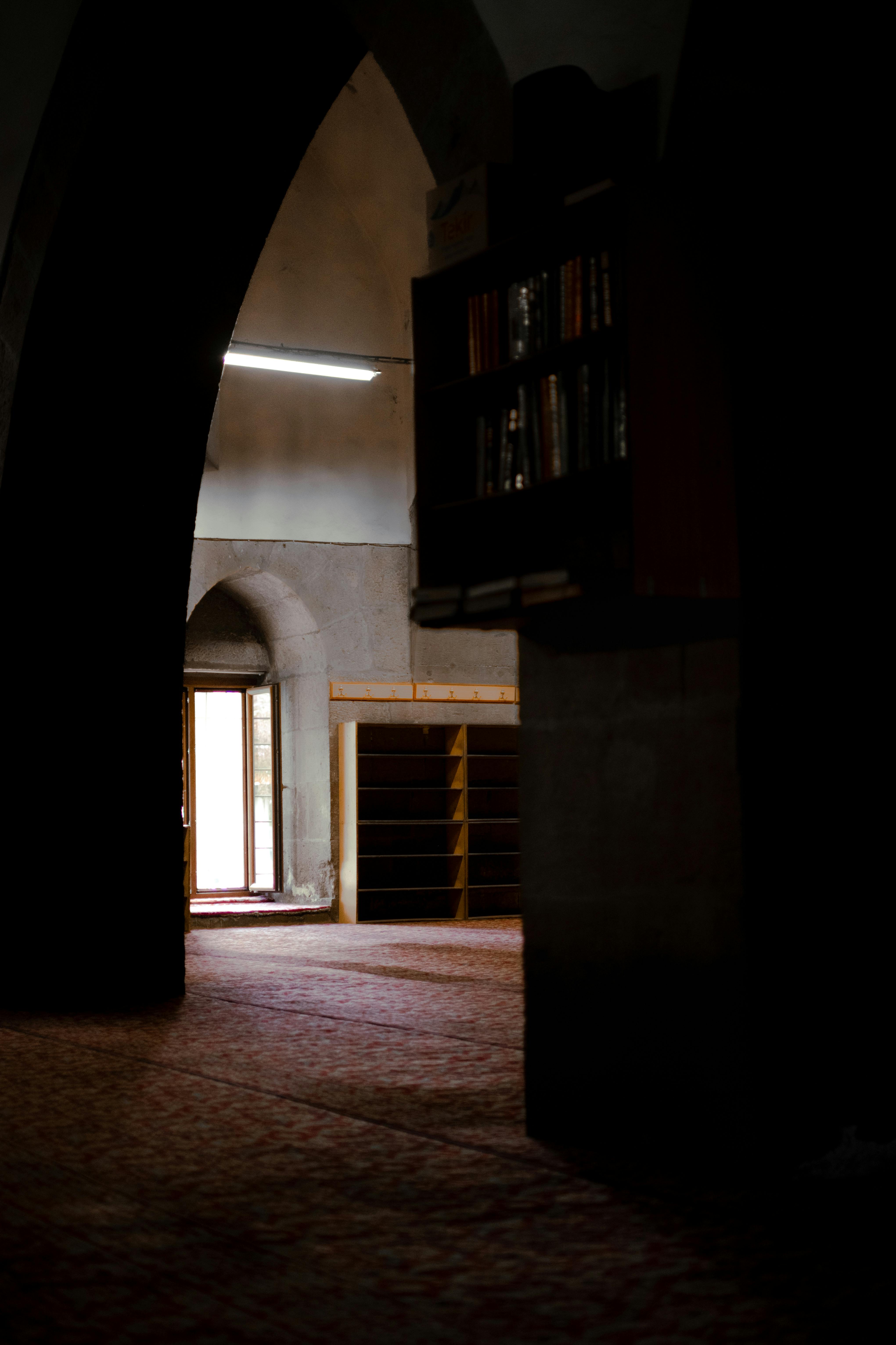 Dimly lit interior of a mosque in Kayseri, Türkiye, featuring arches and carpets.
