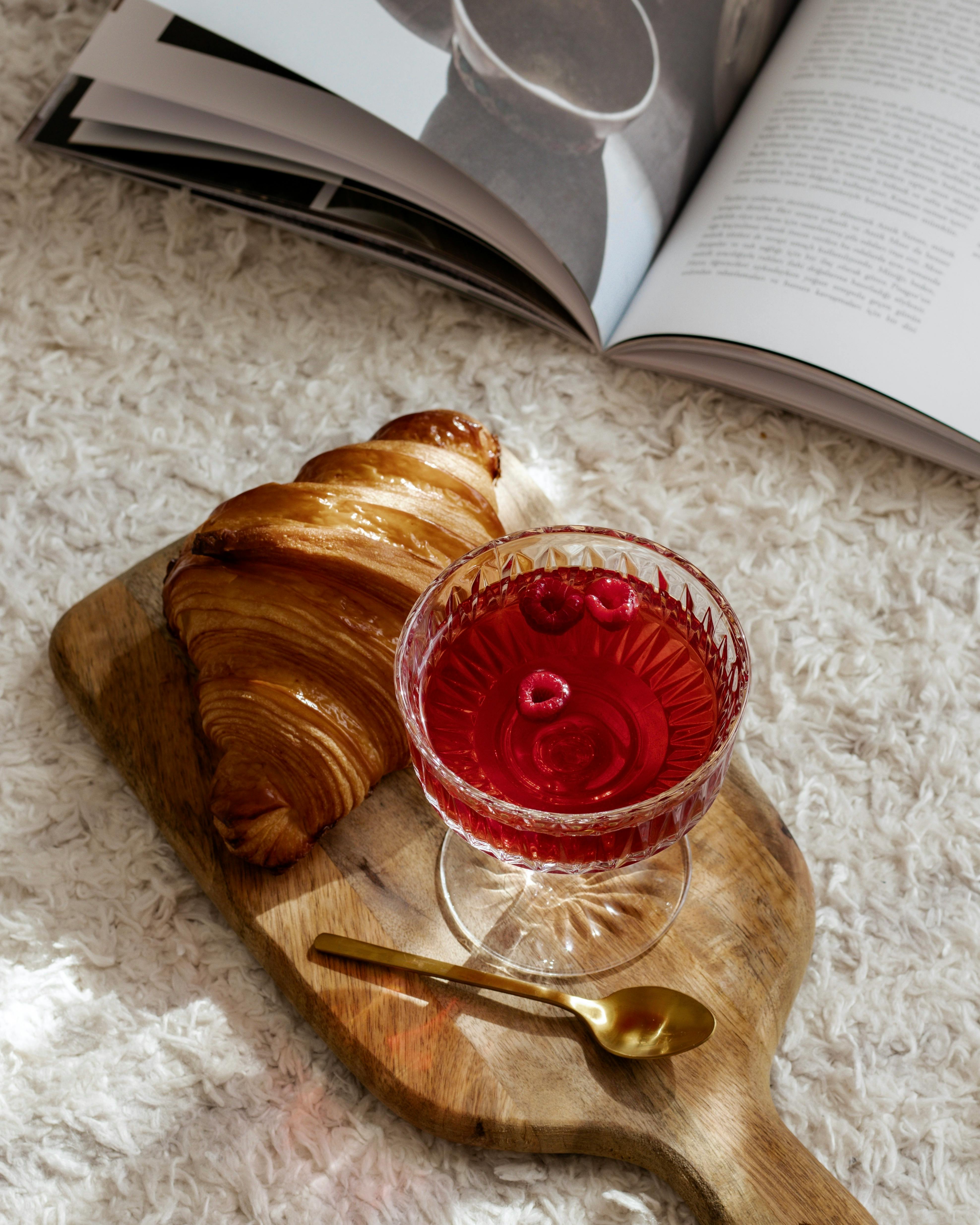 Stylish breakfast setup featuring a croissant and raspberry juice on a wooden board.