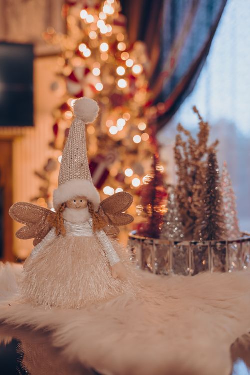 Free Elegant angel doll with wings in a cozy Christmas setting by the tree. Stock Photo