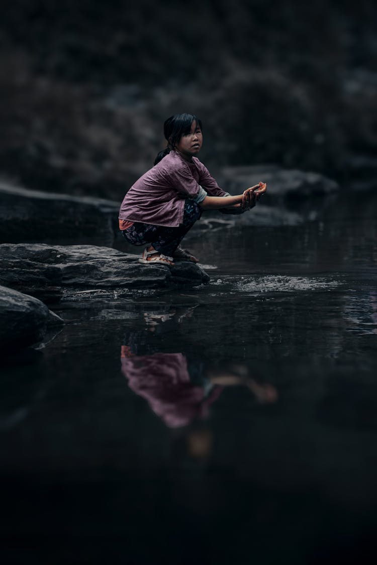 A Girl Crouching On The Riverbank 