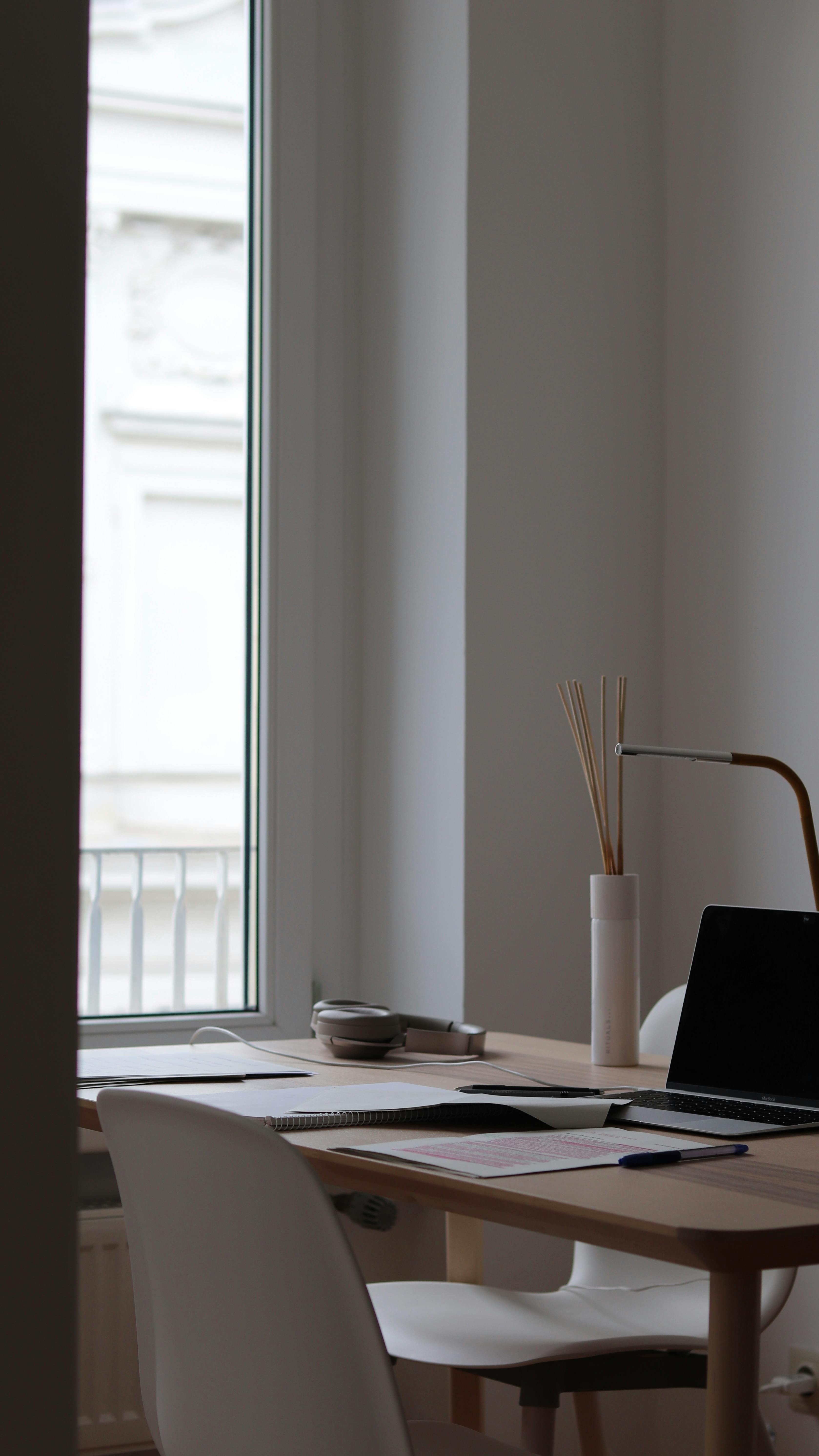 A bright and organized minimalist home office setup with a laptop, desk, and chair by the window.