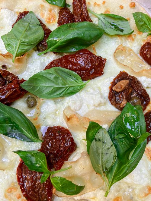 Free A close-up of a gourmet four cheese pizza topped with fresh basil and sun-dried tomatoes. Stock Photo