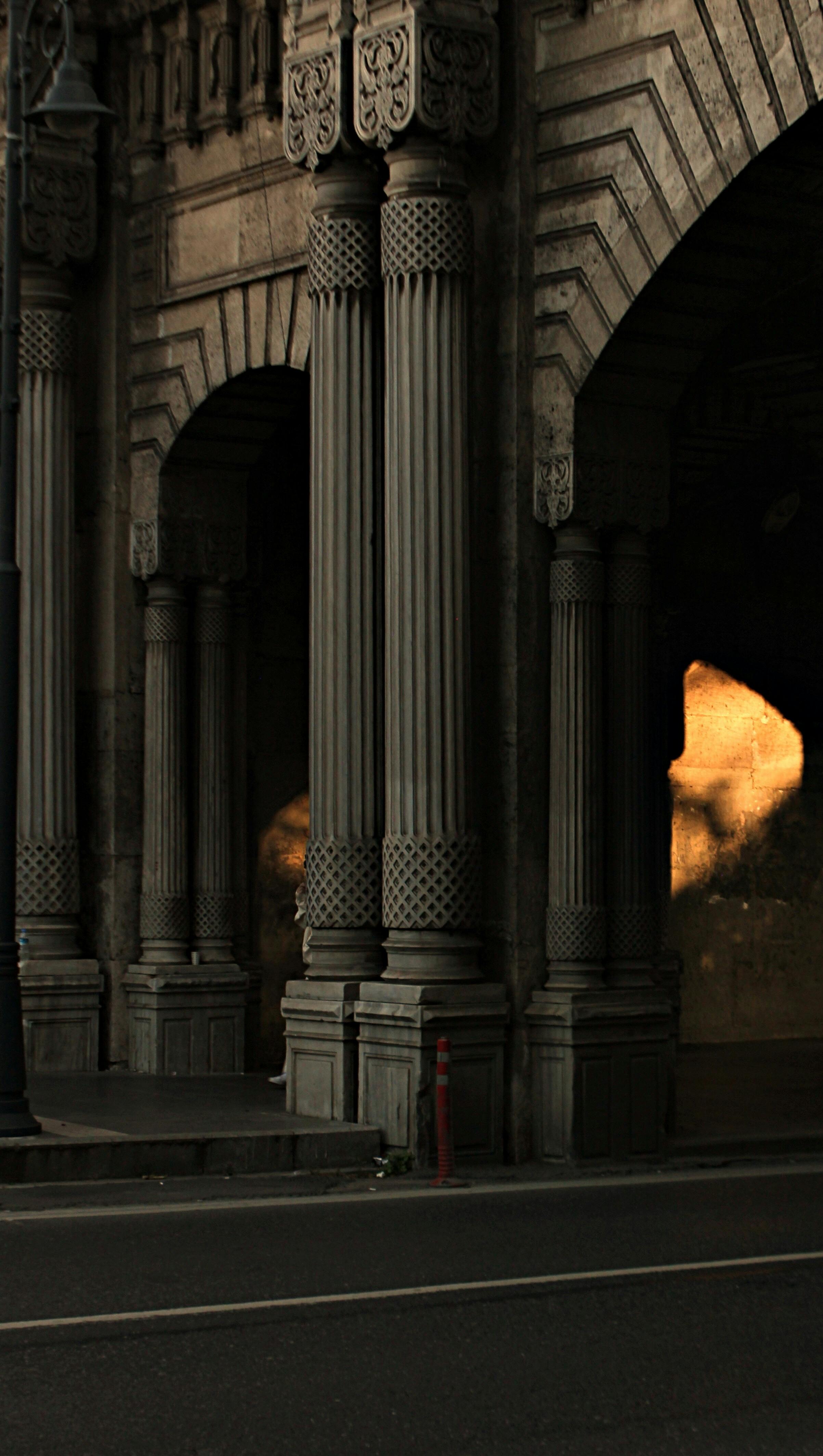 Intricately carved columns and arches cast in evening shadow create a dramatic urban scene.