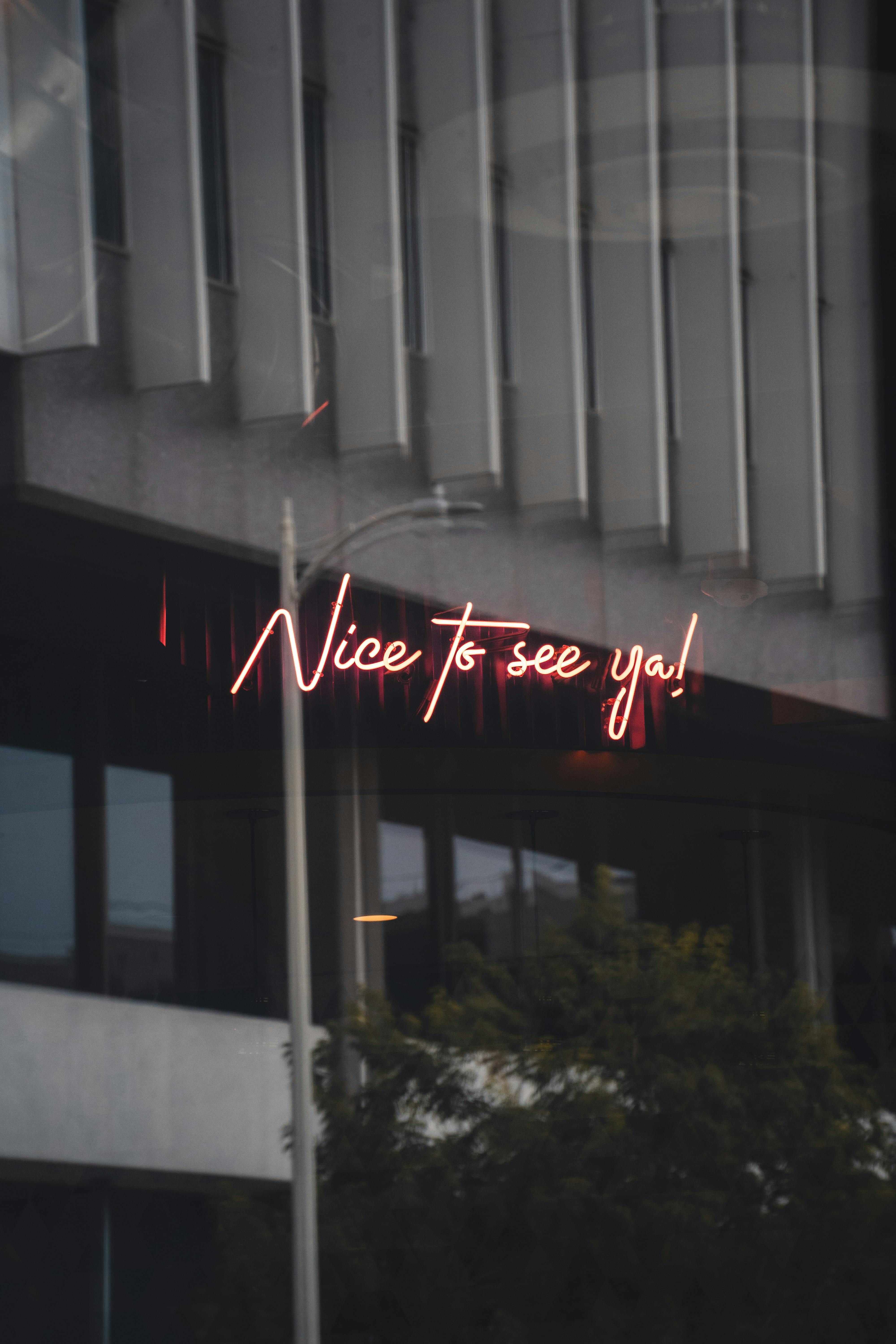 A glowing neon sign reading 'Nice to see ya!' set against an urban building backdrop, creating a welcoming nightlife ambiance.