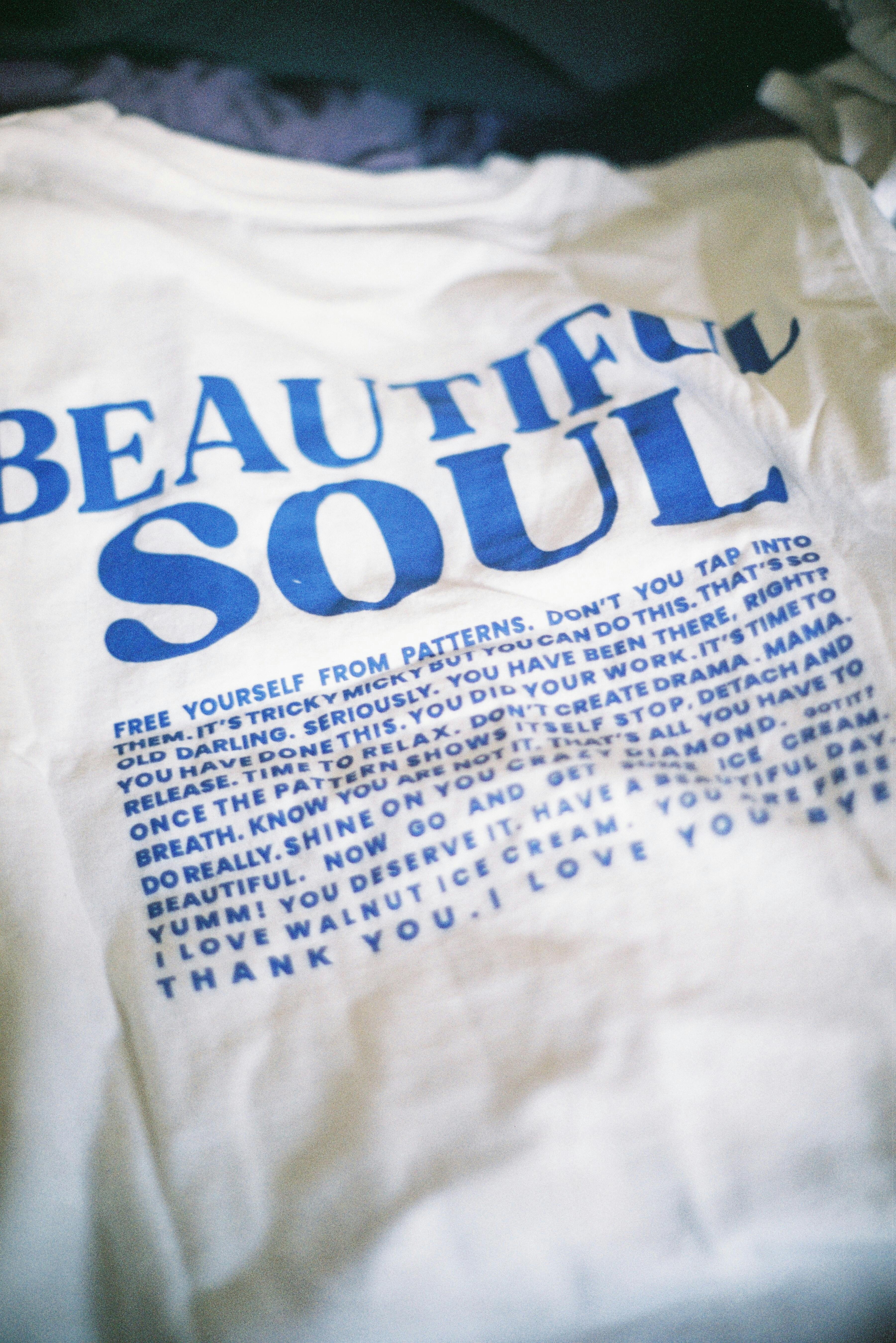 Close-up of a white T-shirt with blue inspirational text reading 'Beautiful Soul.'